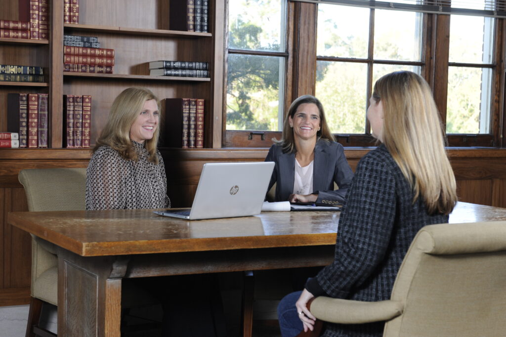 Three women sitting at a table with a laptop.